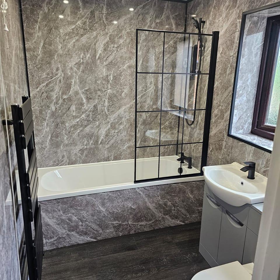 Modern marble-effect bathroom with bath and black framed shower screen by JD Plumbing & Bathrooms
